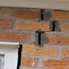 A brick wall displaying stair-step cracks and messy tuckpointing on a Woonsocket home